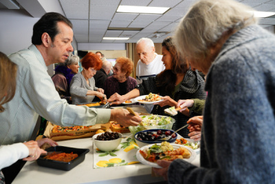 Image shows congregation members gathering around a kitchen island full of food, filling their plates.