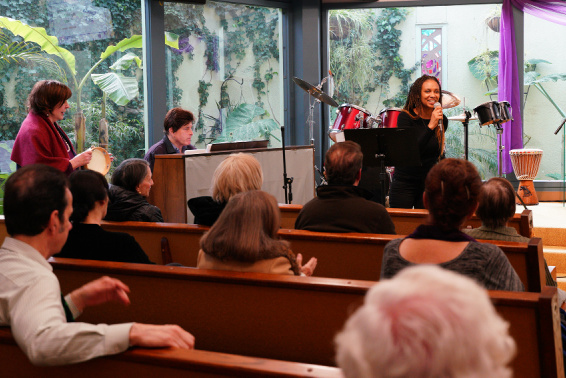 Image is our sanctuary during a Sunday service. The pews are full of people. Jamila Ford sings into a microphone.