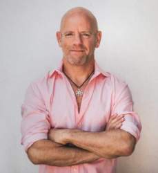 Image is Gahl Sasson wearing a pink shirt with his arms crossed in front of him.