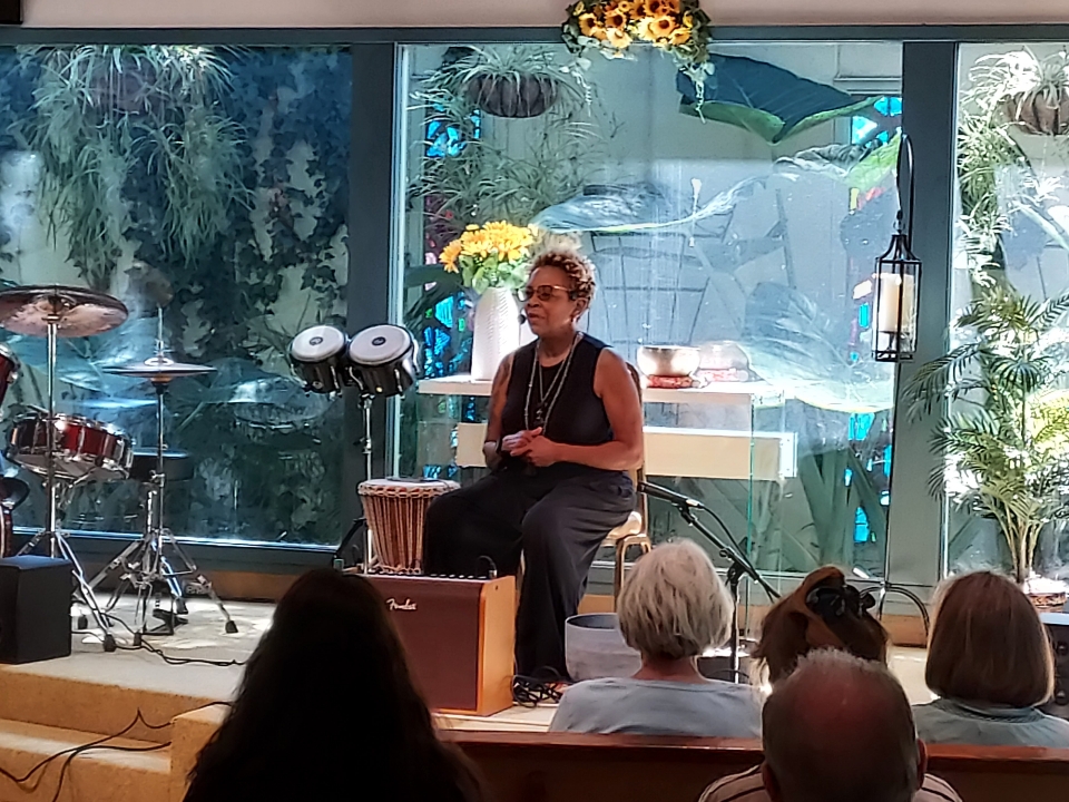 Image is Phyllis Douglass sitting in the Unity of Pasadena sanctuary in front of an audience.
