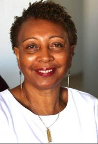 Photo is a headshot of Teresa Morris, smiling, wearing a white shirt, gold necklace and earrings.