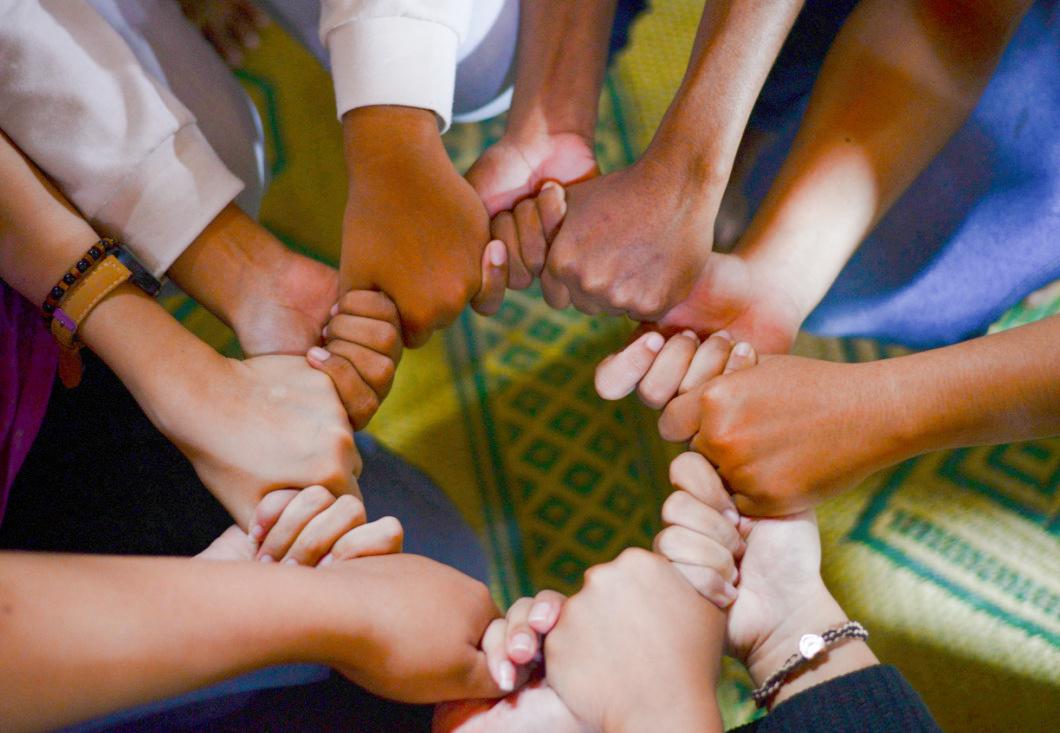 Image shows hands of people with different colored skin holding each other to make a circle.