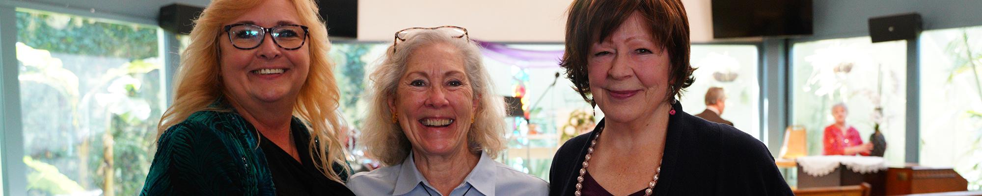 Three prayer chaplains stand together smiling in front of the sanctuary