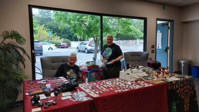 Image shows a table with lots of different crystals displayed. Steph and Sarah Darshan from Lighthouse Crystals are smiling.